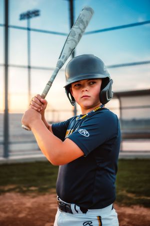 Youth baseball batter in Rawlings helmet holding bat in ready stance at sunset.