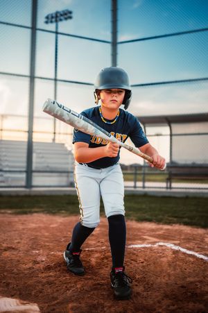 Young baseball player in navy uniform holding bat at home plate at sunset.