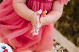Close-up of baby hands covered in frosting in pink tulle dress.