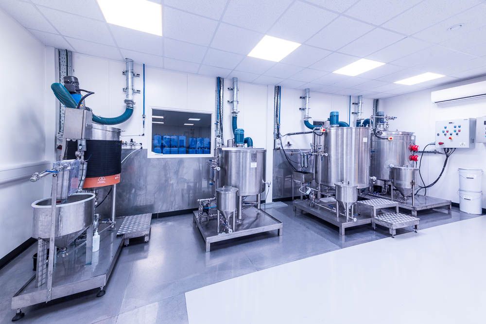 Stainless steel pharmaceutical mixing tanks and processing equipment in a clean white laboratory facility.