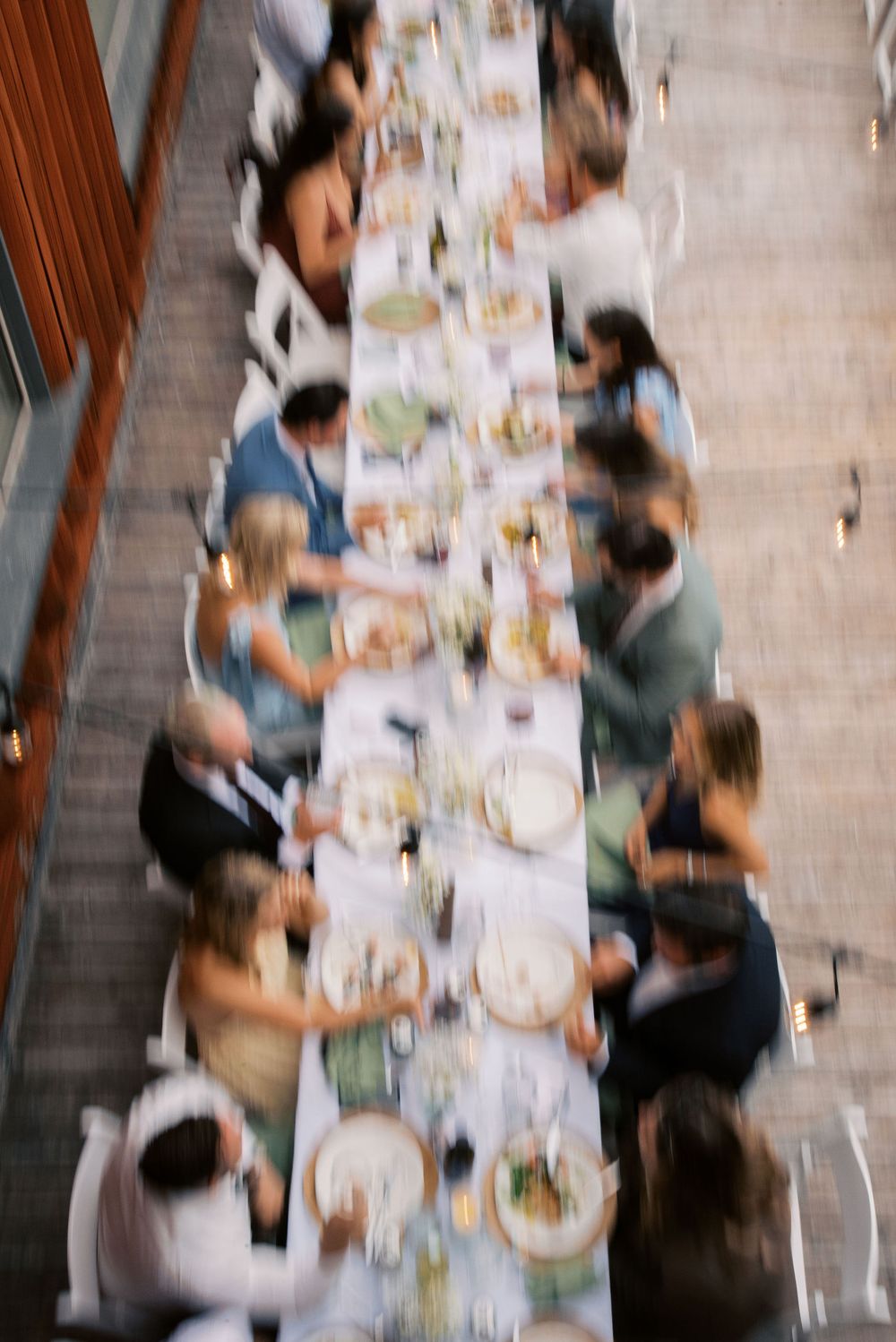 Aerial view of wedding reception guests dining at a long decorated table with floral centerpieces.