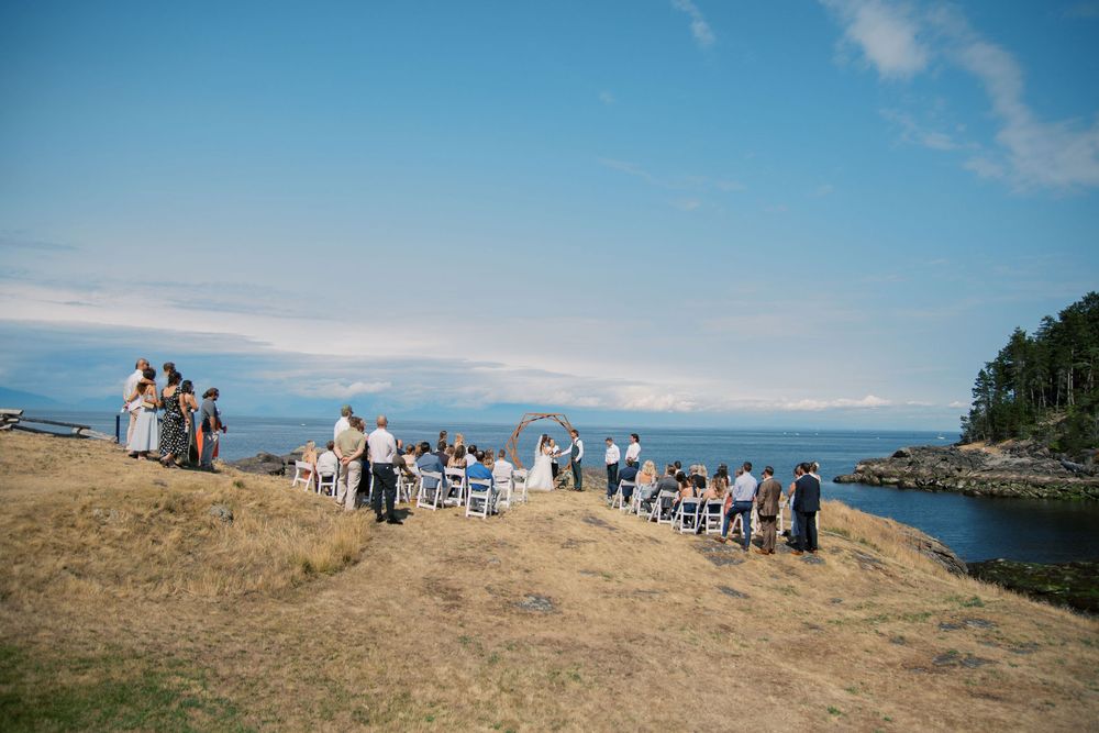 Outdoor wedding ceremony on a coastal bluff overlooking the ocean on a sunny day.