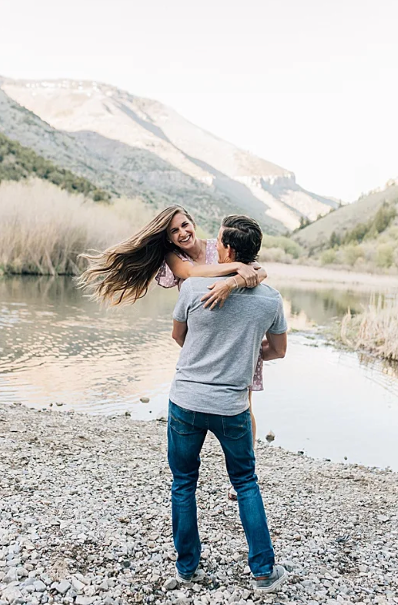 Loving couple sharing a joyful embrace by a serene mountain lake surrounded by scenic landscape.