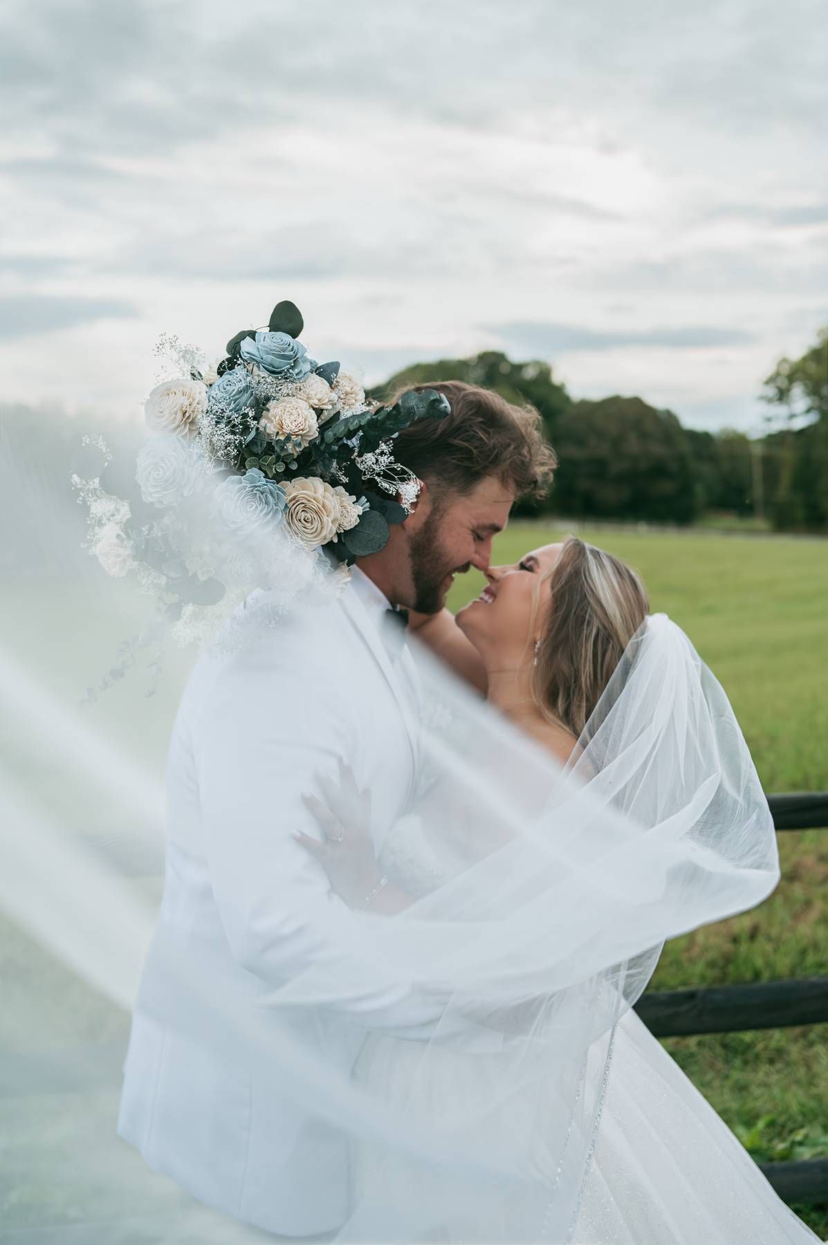 Couple in matching black wedding attire sharing a romantic kiss outdoors with white bouquet in North Carolina