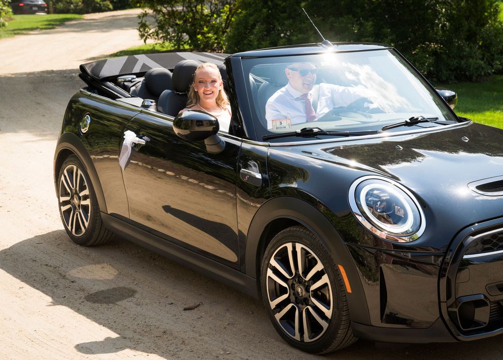 Bride and groom riding in a black Mini Cooper convertible on their wedding day.
