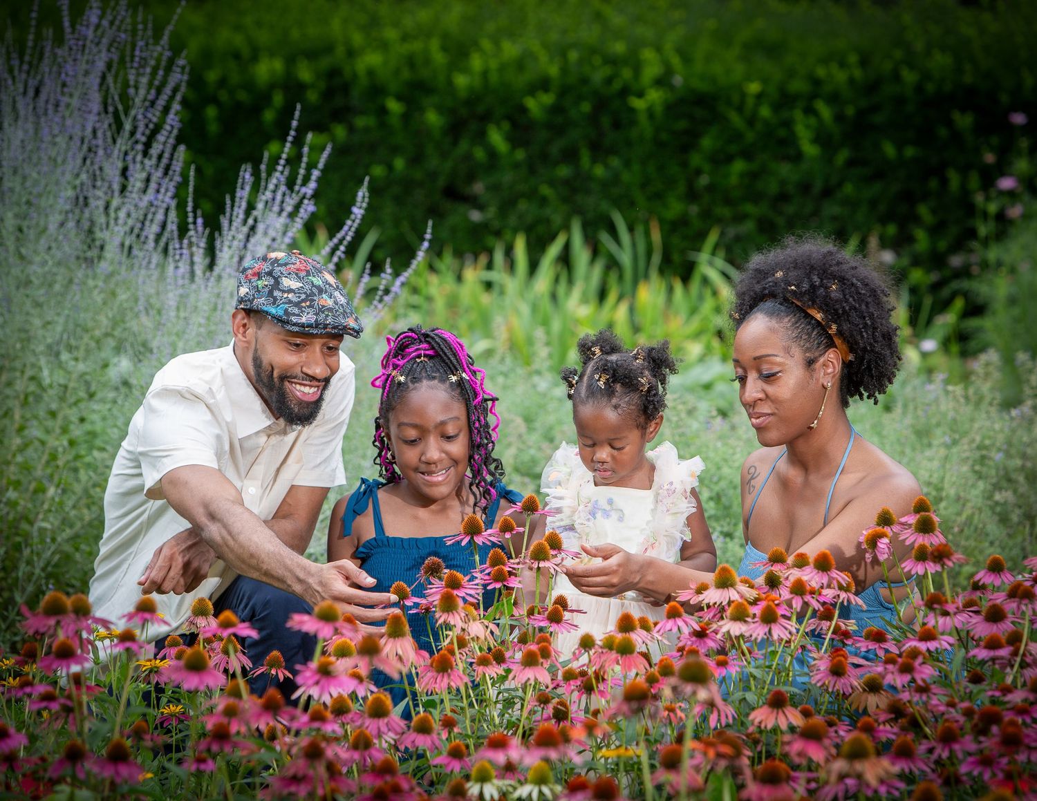 A joyful Black family with two young daughters explores vibrant pink echinacea flowers in a lush garden.