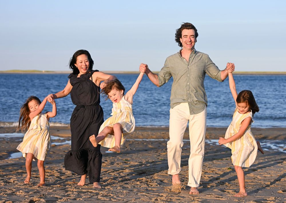 Happy family of five playing on a sandy beach at sunset, parents swinging children while holding hands.
