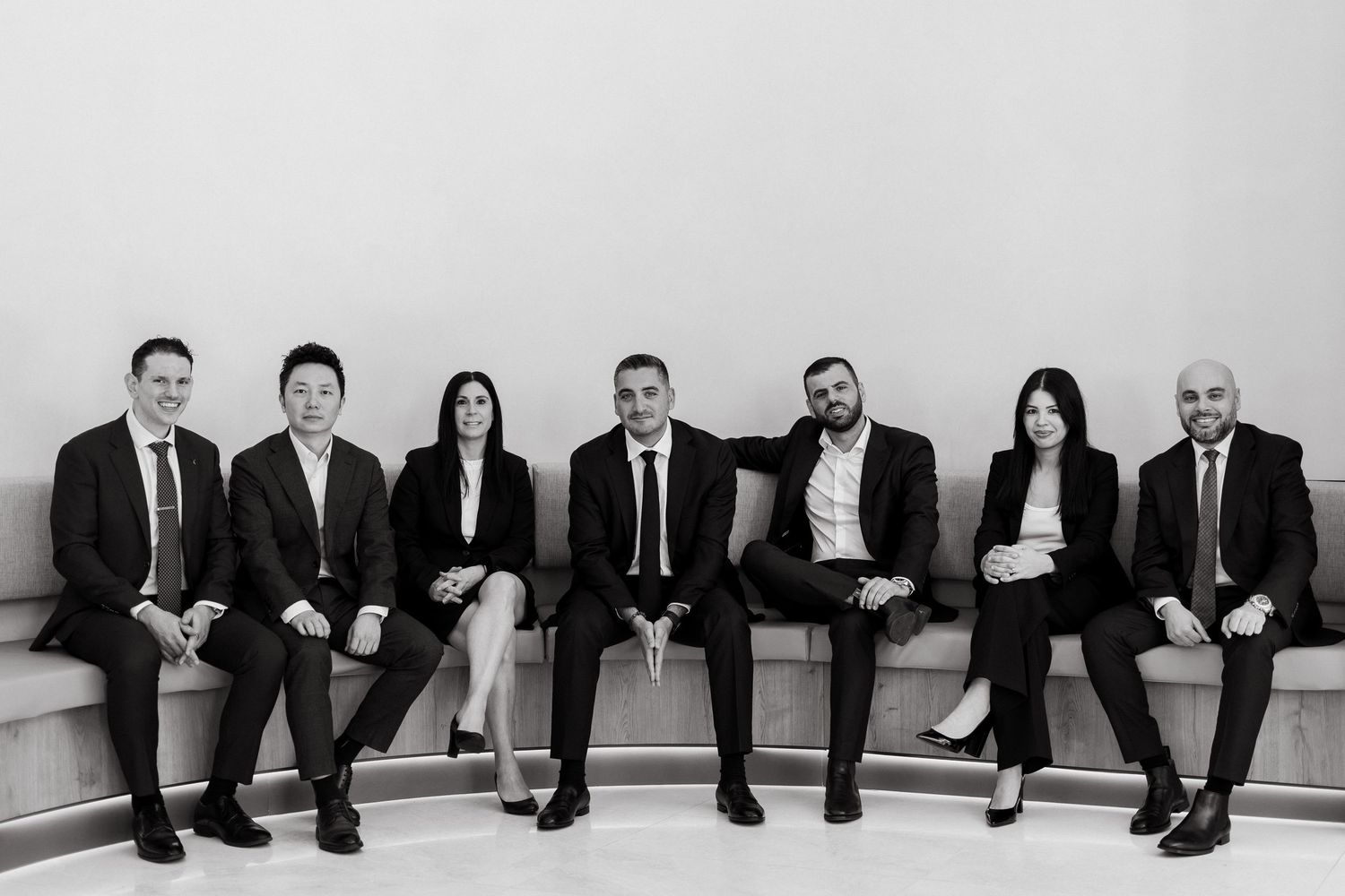 Black and white professional group photo of seven business executives in formal attire seated together.