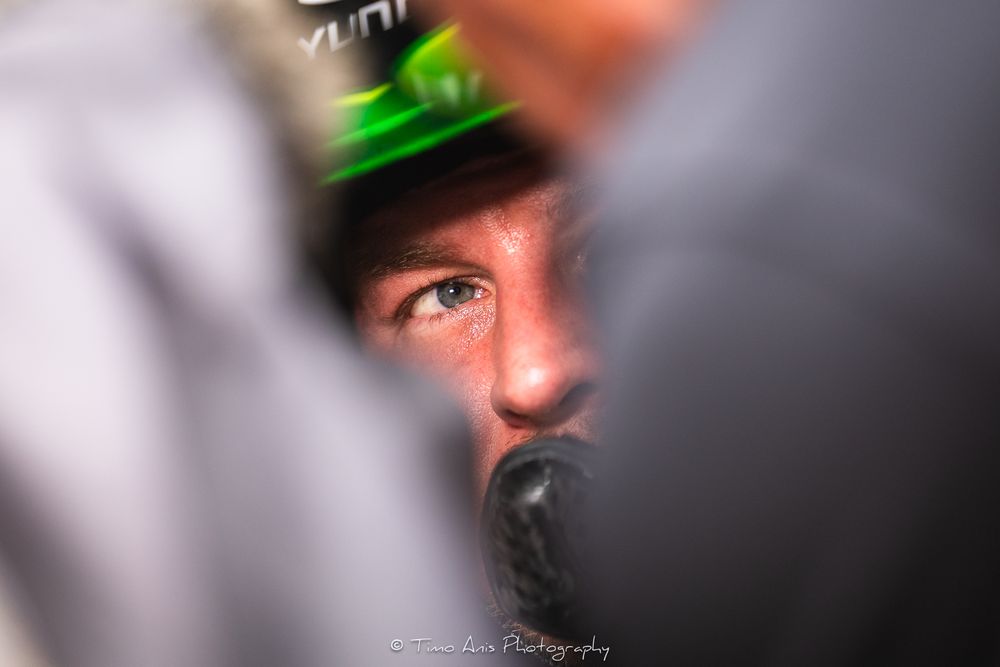 Close-up of a focused male racing driver wearing a green helmet, captured with shallow depth of field.