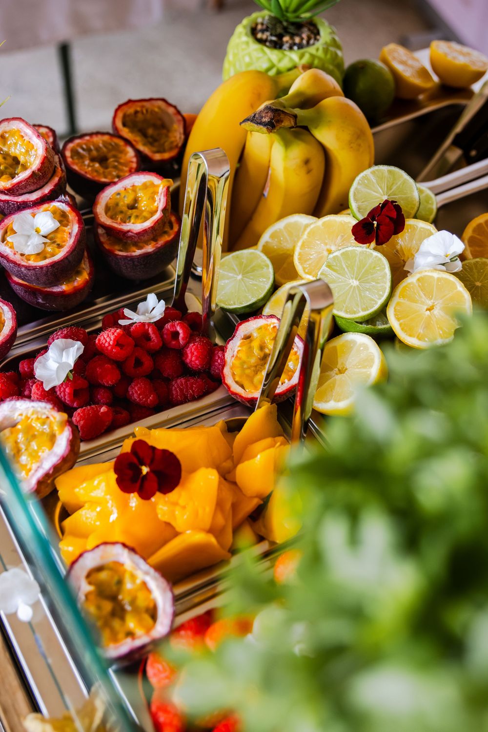 Colorful tropical fruit display with passion fruit, bananas, limes, raspberries, and mango slices at a buffet.