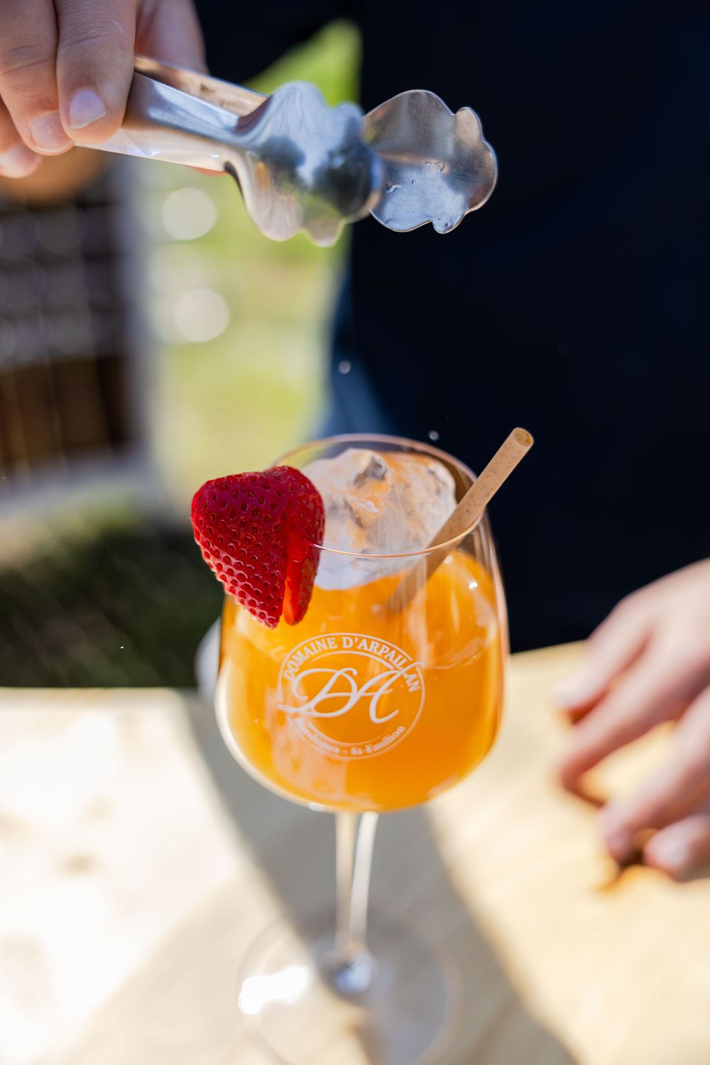 Elegant cocktail with orange juice, ice cream scoop, and fresh strawberry garnish in a branded wine glass outdoors.