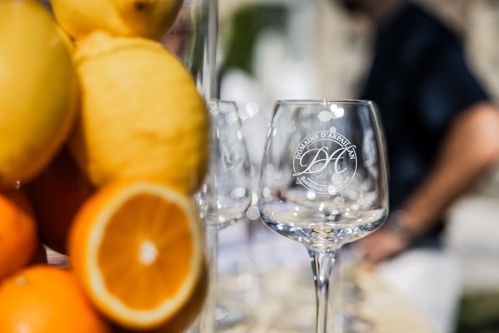 Elegant wine glasses with DC monogram logo beside fresh lemons and oranges at an outdoor event.