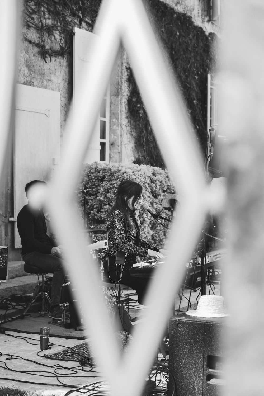 Black and white photo of musicians performing outdoors, viewed through a diamond-shaped gate.