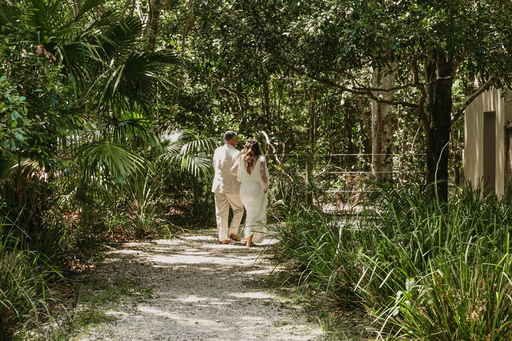 Bride and father walking hand in hand through lush gardens after their romantic Byron Bay wedding ceremony.