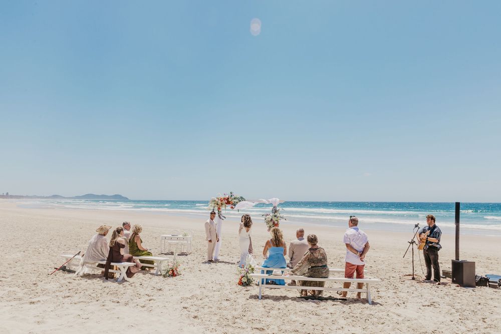 Guests watching an intimate Byron Bay beach wedding ceremony with ocean views and a beautifully styled floral arbour.