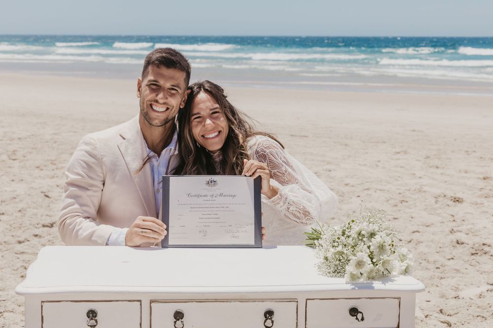 Bride and groom smiling after signing their marriage certificate during a beautiful Byron Bay beach wedding ceremony.