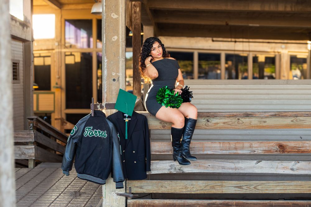Woman in black outfit and boots sits on wooden steps with a Jets jacket and luggage nearby.