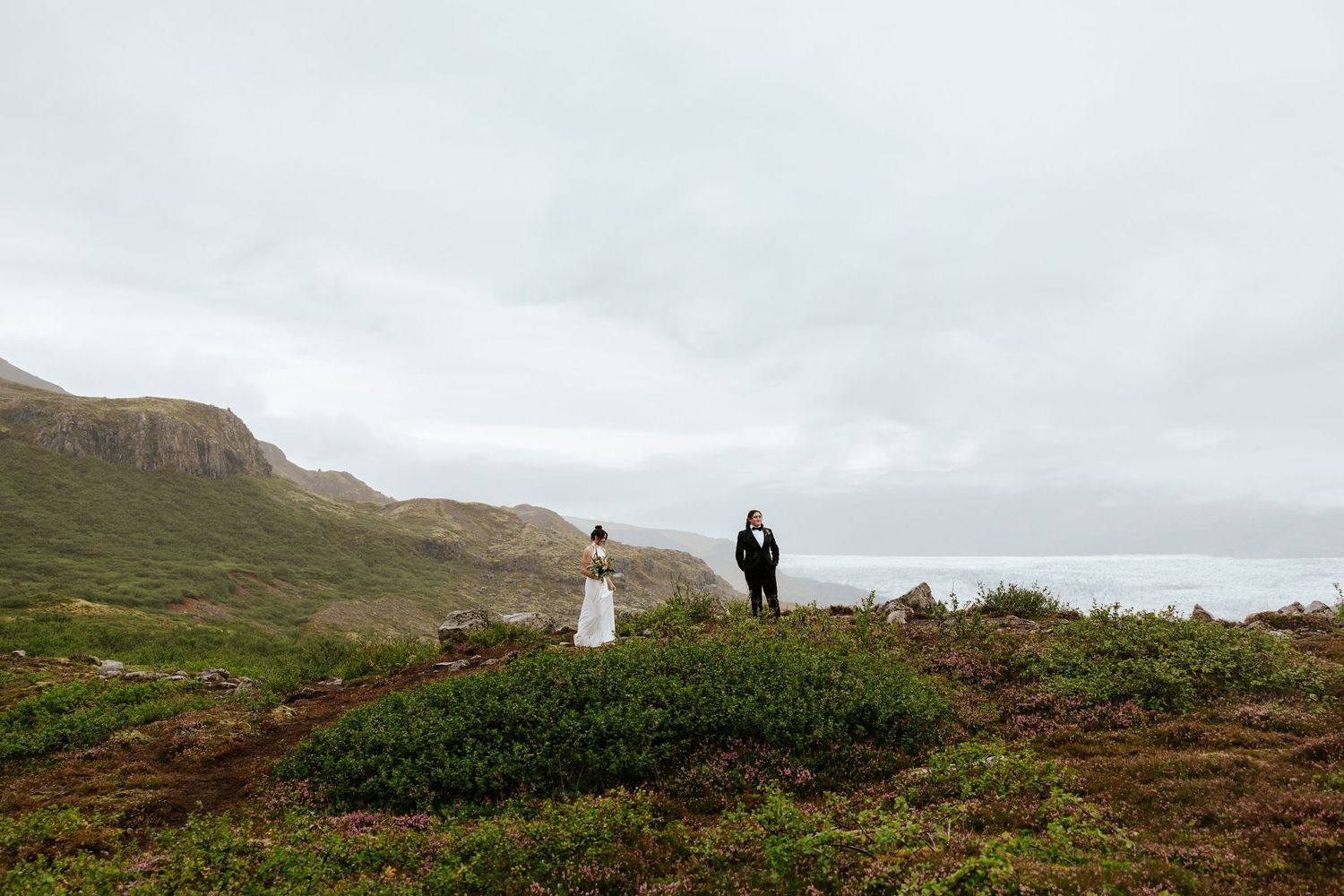 bride walking up to her bride for a first look at Mulagljufur Canyon, Iceland with mountains in the back during their elopement in Iceland