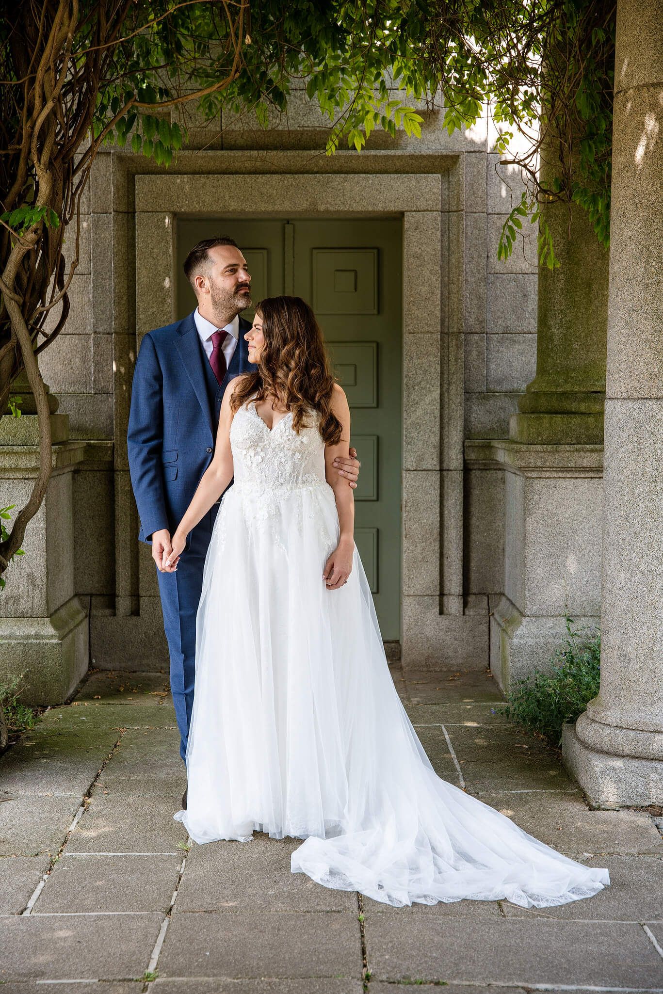 Bride in a white tulle gown and groom in a blue suit embrace at Dublin city park photo by AK wedding photography.