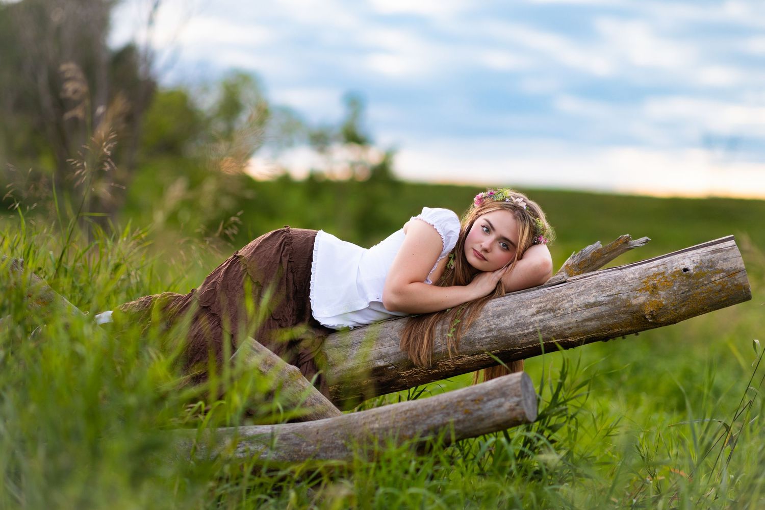 A Senior girl relaxes on a fallen tree trunk in a lush green meadow on a sunny summer day in Hinton, Iowa.