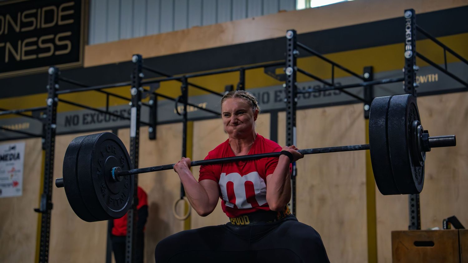 CrossFit athlete in an M&M costume grinds up a front squat under the Ironside Fitness sign in Janesville, WI, face straining at a comp.