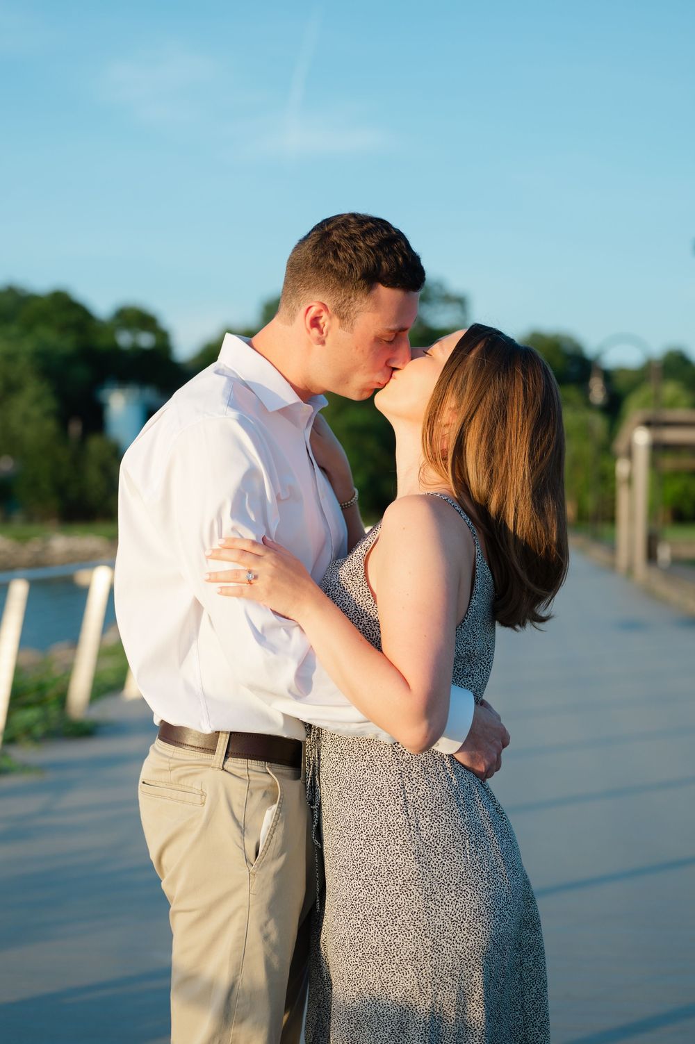 Couple sharing a romantic kiss on a wooden bridge at golden hour, woman wearing a sparkly dress.