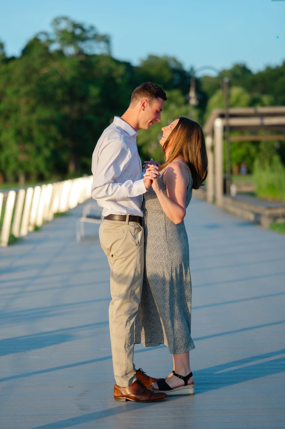 Couple dancing together on wooden bridge path surrounded by lush green trees at golden hour.