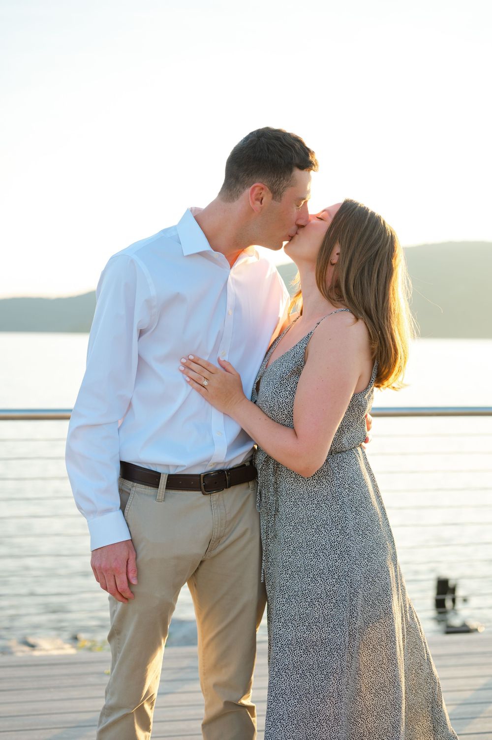 Couple sharing a romantic kiss on a waterfront deck at golden hour during their engagement session.