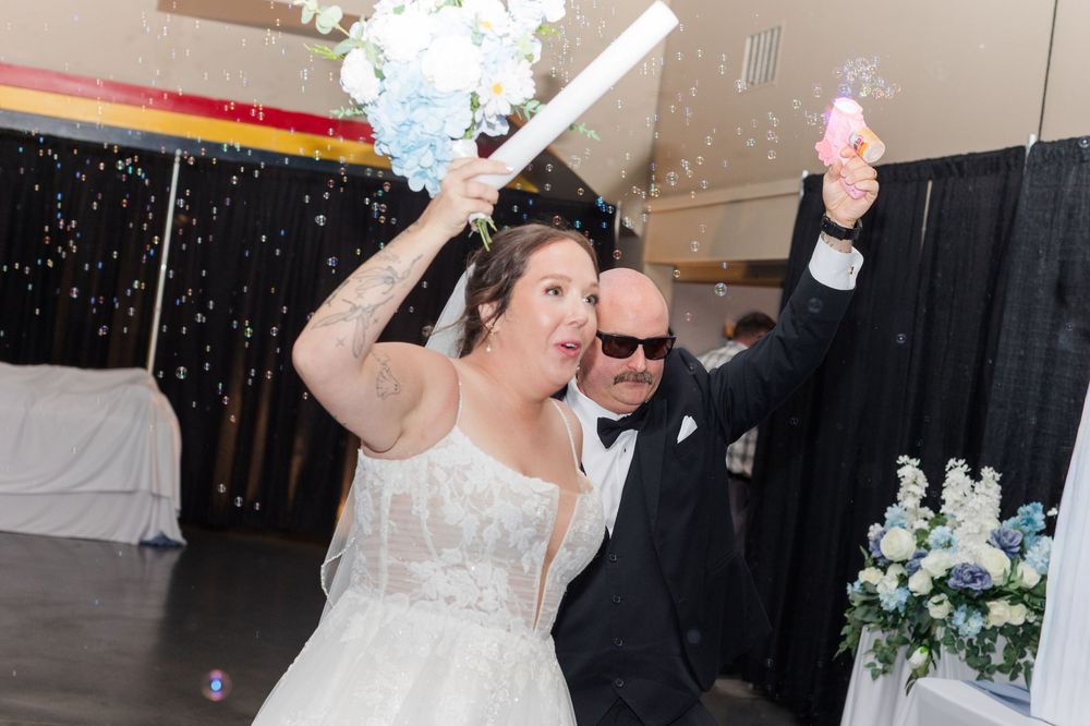 Bride and groom celebrating wedding reception entrance with confetti poppers, bride in white gown holding blue bouquet.