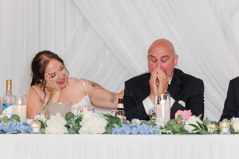 Bride and groom sharing an emotional moment at wedding reception table adorned with blue hydrangeas and candles.