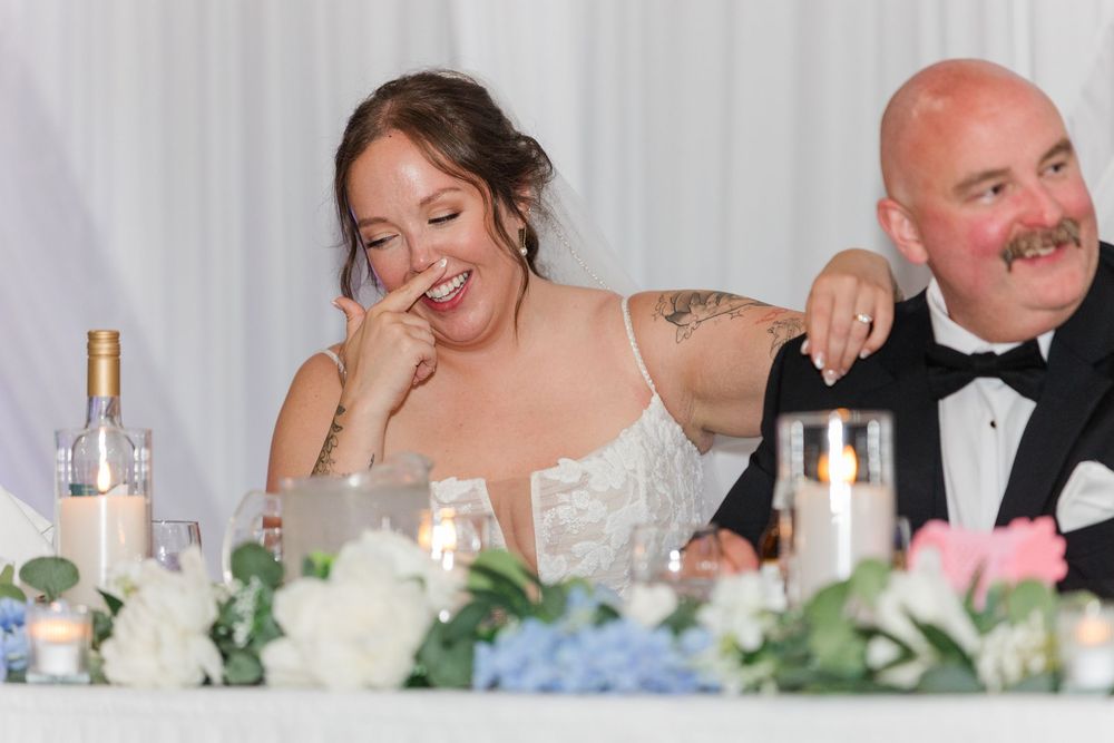 Bride and groom laughing joyfully at wedding reception head table adorned with candles and floral arrangements.