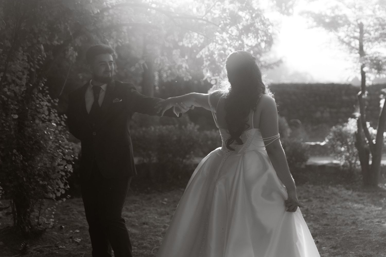 Black and white photo of bride and groom dancing outdoors in garden setting.