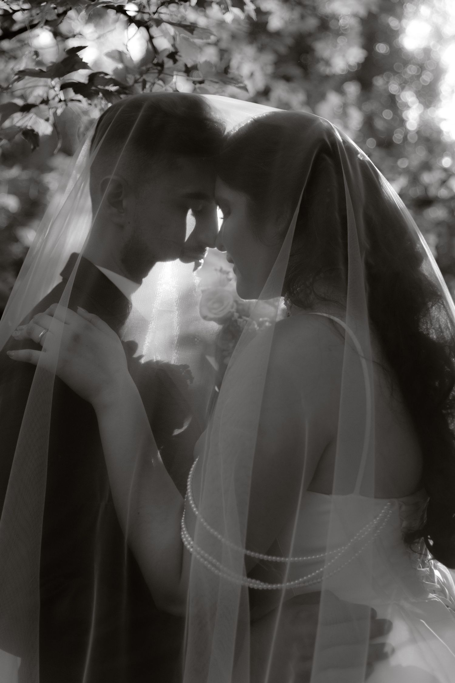 Black and white romantic photo of bride and groom under veil touching foreheads.