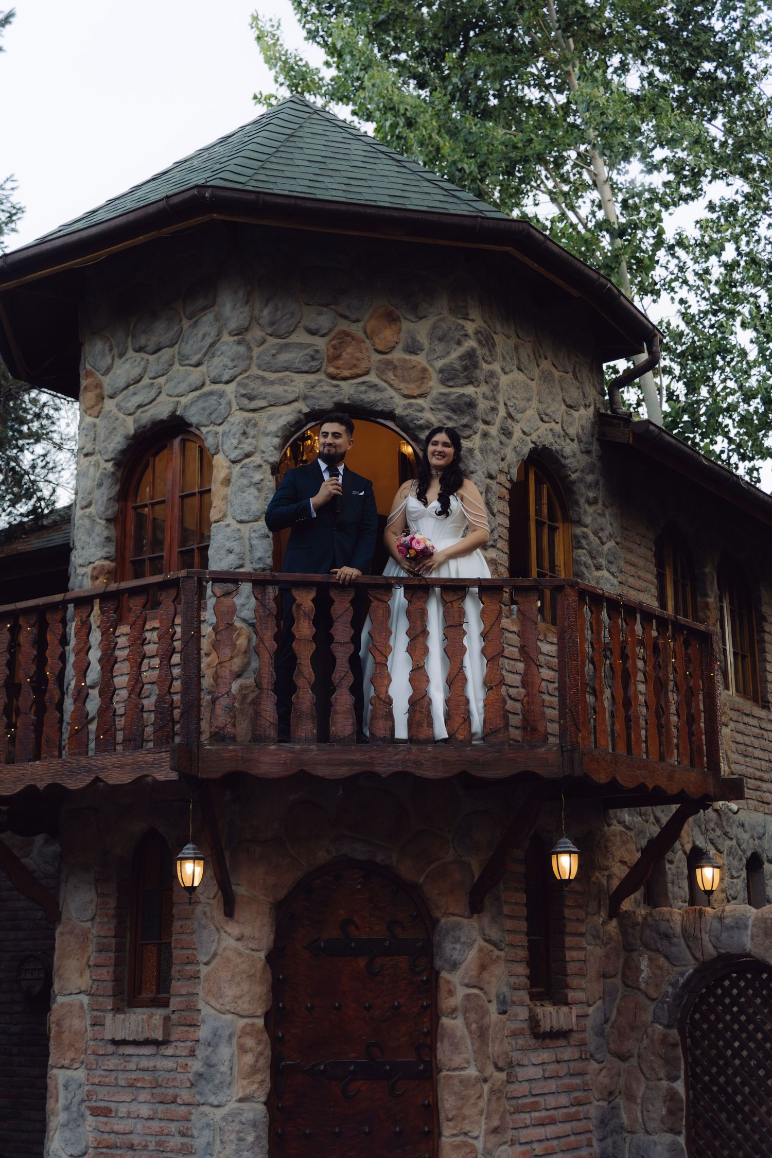 Elegant bride and groom stand together on a stone castle balcony during their outdoor wedding celebration.