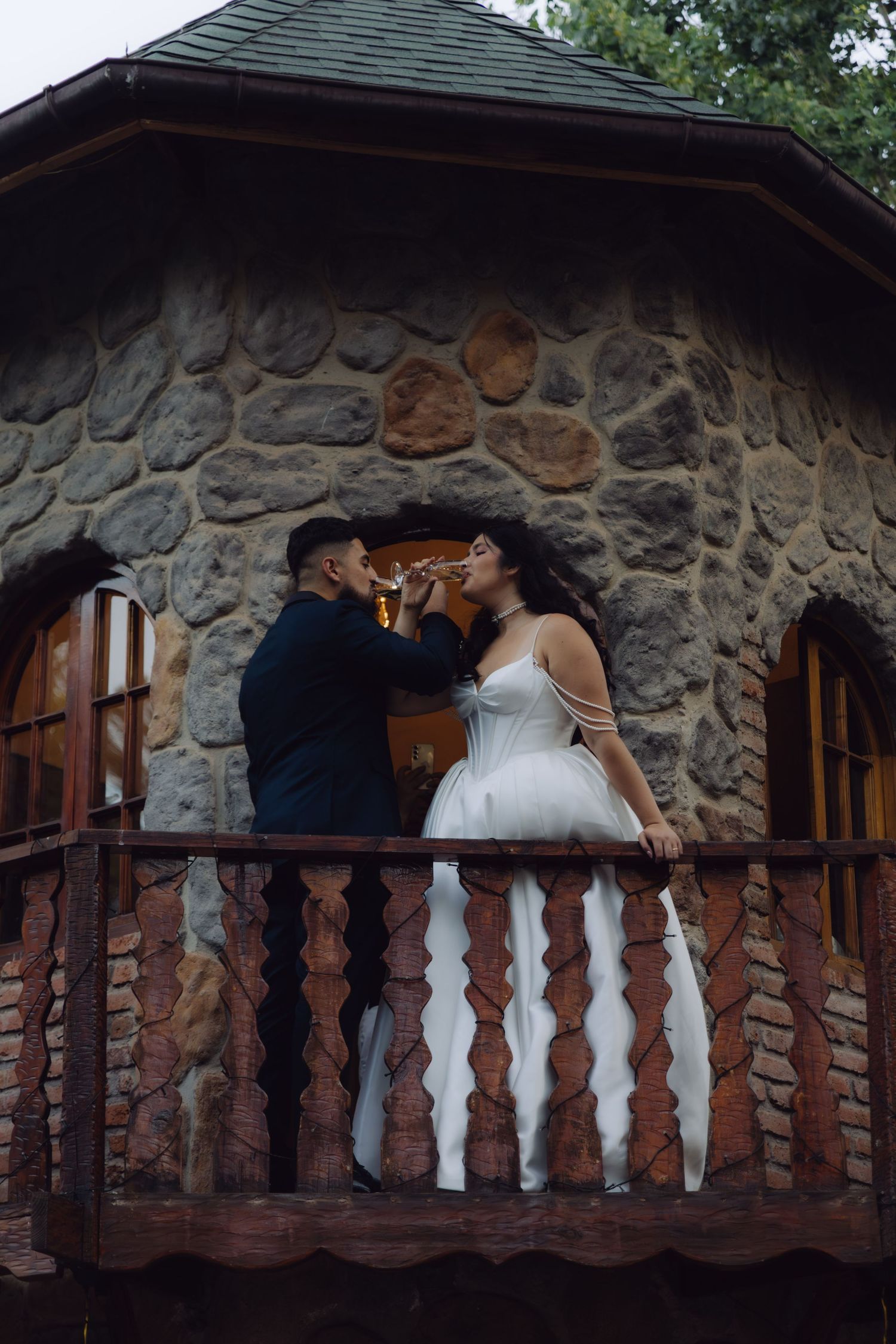 Bride and groom share a champagne toast kiss on the balcony of a stone castle wedding venue.