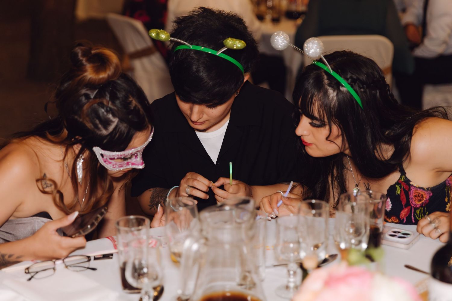 Three wedding guests in party headbands gathered closely together at decorated reception table.