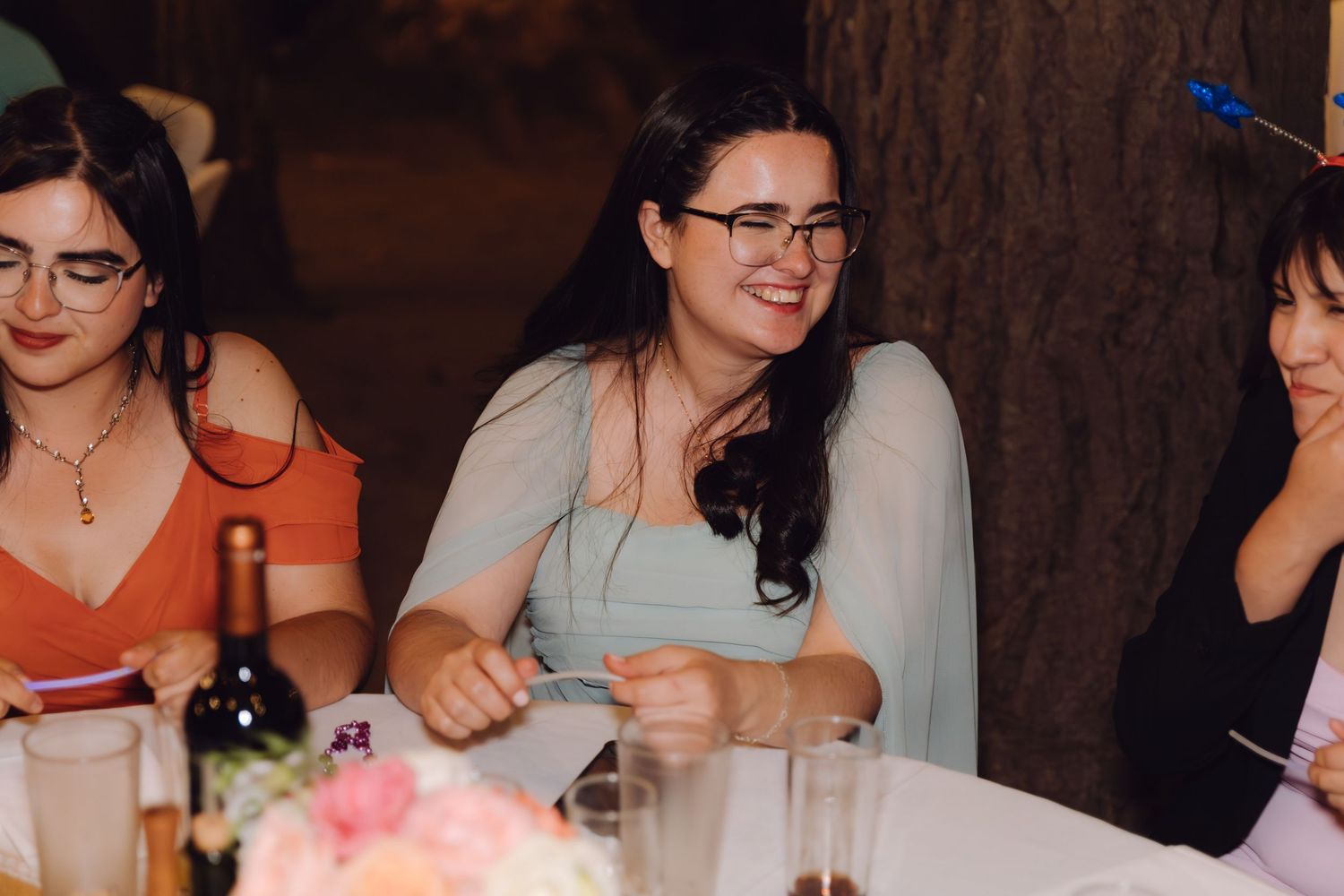 Smiling female wedding guest in light blue dress seated at flower-decorated reception table.