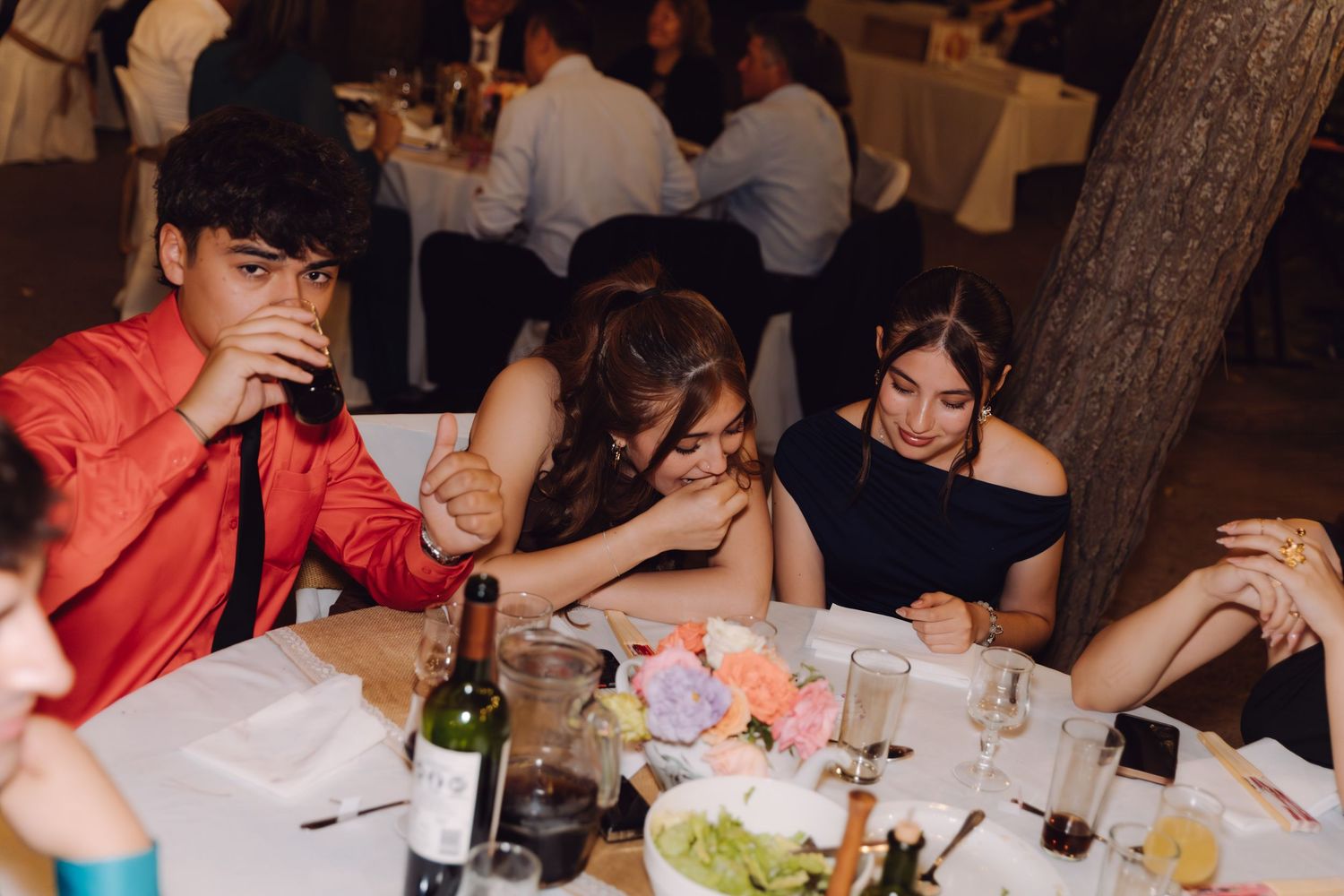 Young wedding guests laughing and socializing at decorated table during evening reception.