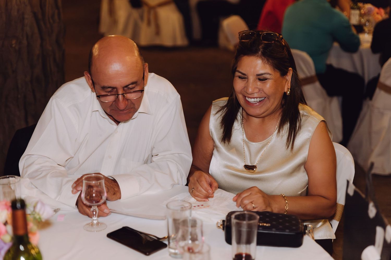 Couple laughing together at a wedding reception dinner table with wine glasses.