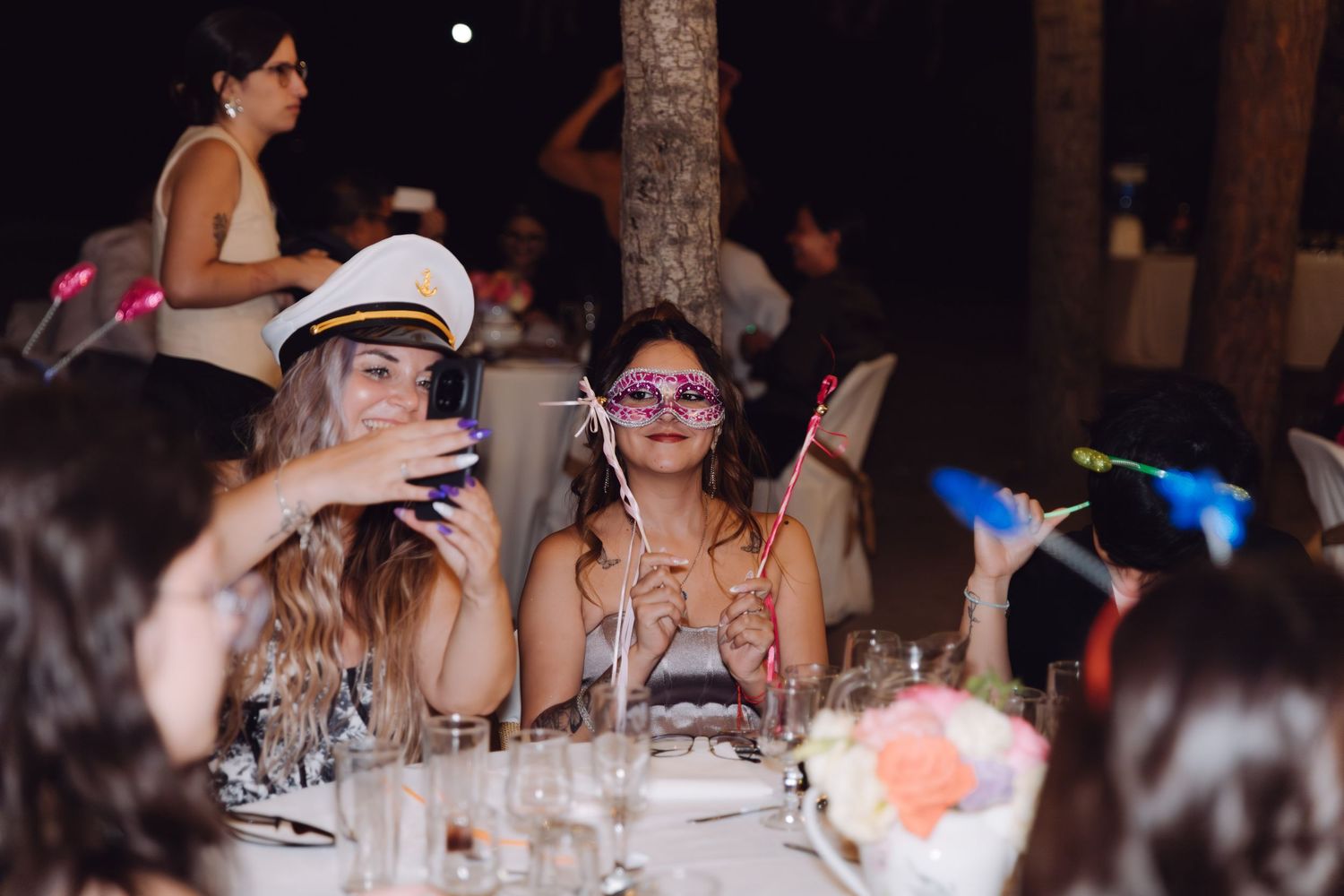Wedding guests wearing fun photo booth props and masks at an outdoor reception.