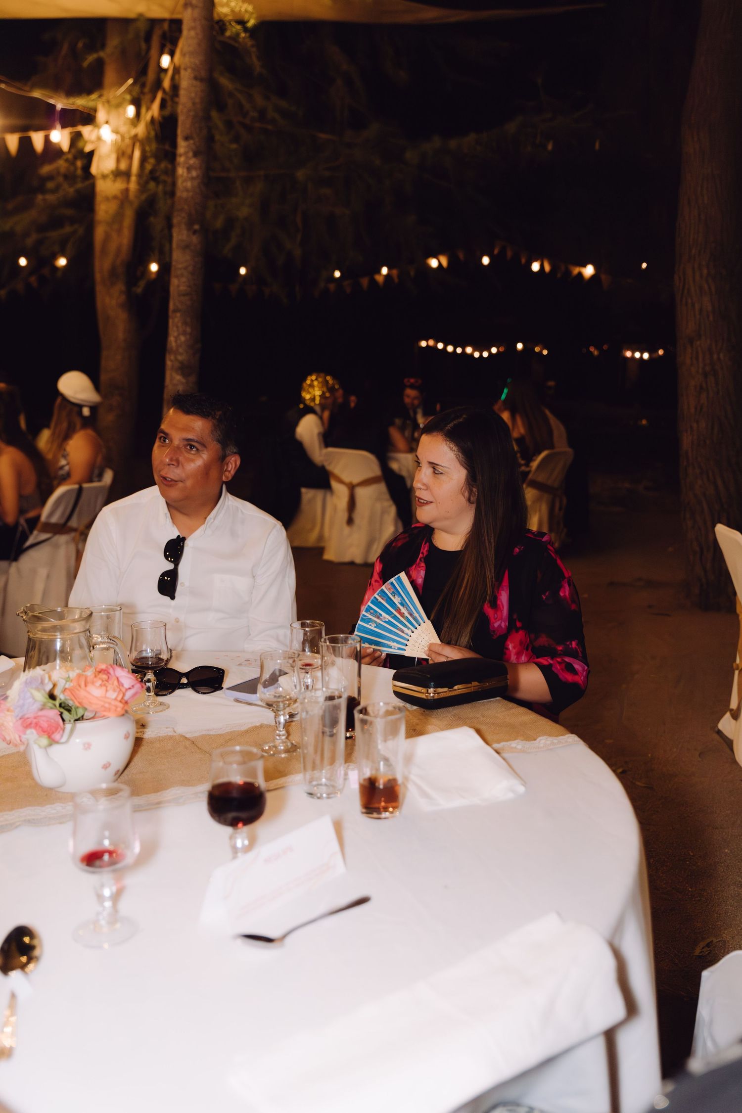 Man and woman sitting at elegantly decorated wedding reception table at night.