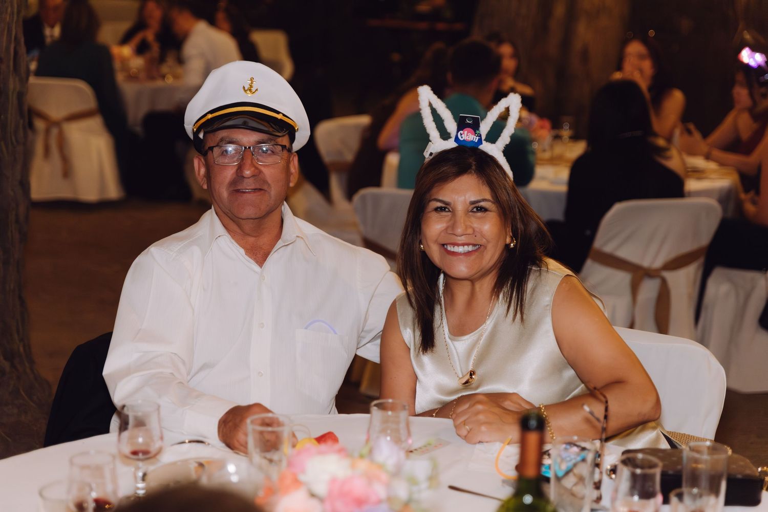 Smiling couple posing at wedding reception wearing captain hat and bunny ears.
