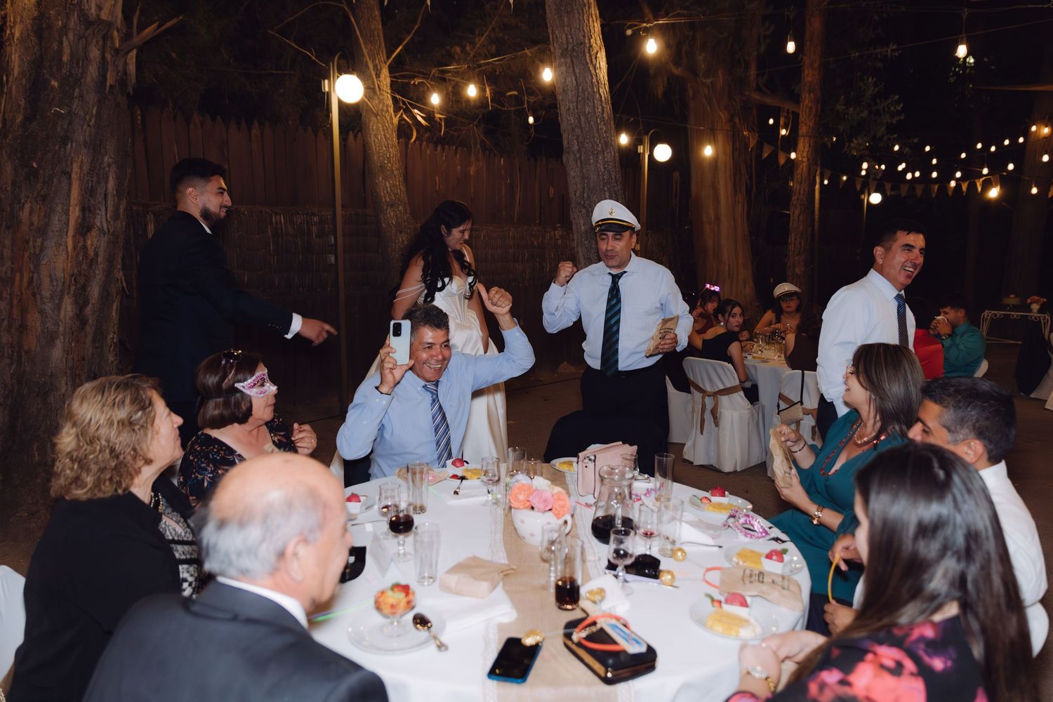 Guests cheering and dancing around a decorated table at an outdoor wedding reception.