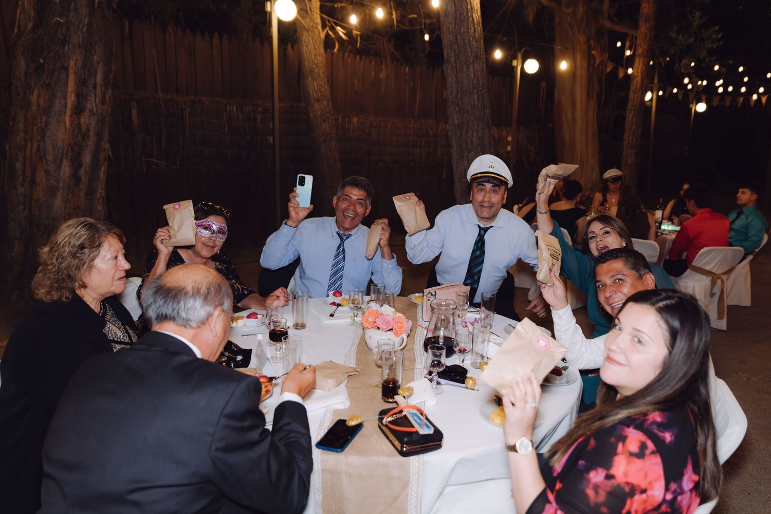 Joyful wedding guests raising hands and phones in celebration at an outdoor reception.