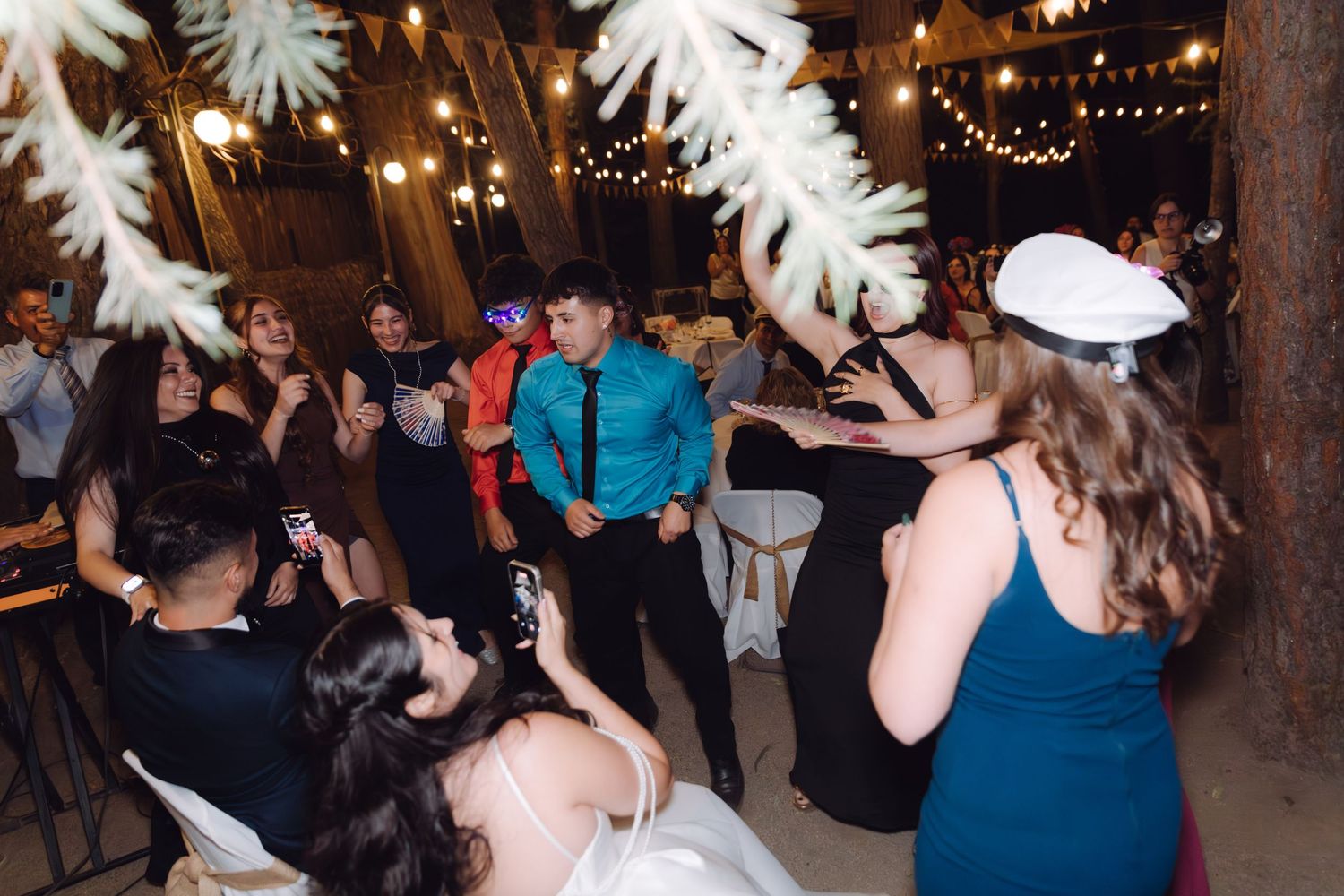 Bride and guests dancing joyfully at indoor wedding reception decorated with white feather trees.