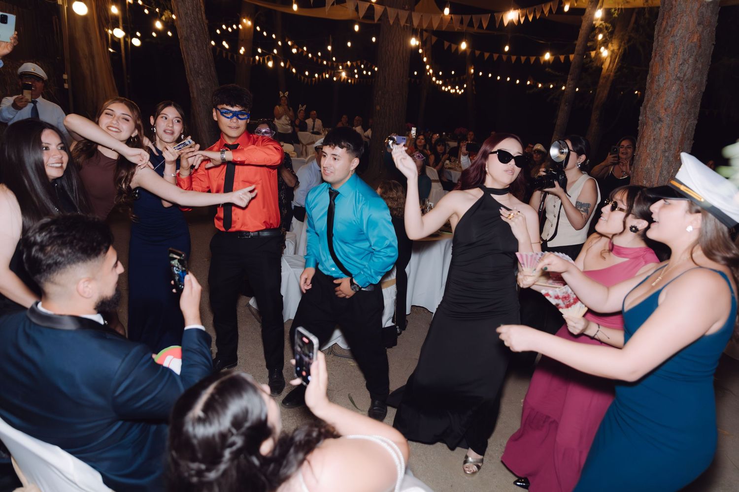 Lively outdoor wedding reception dance floor with guests in formal attire under string lights.