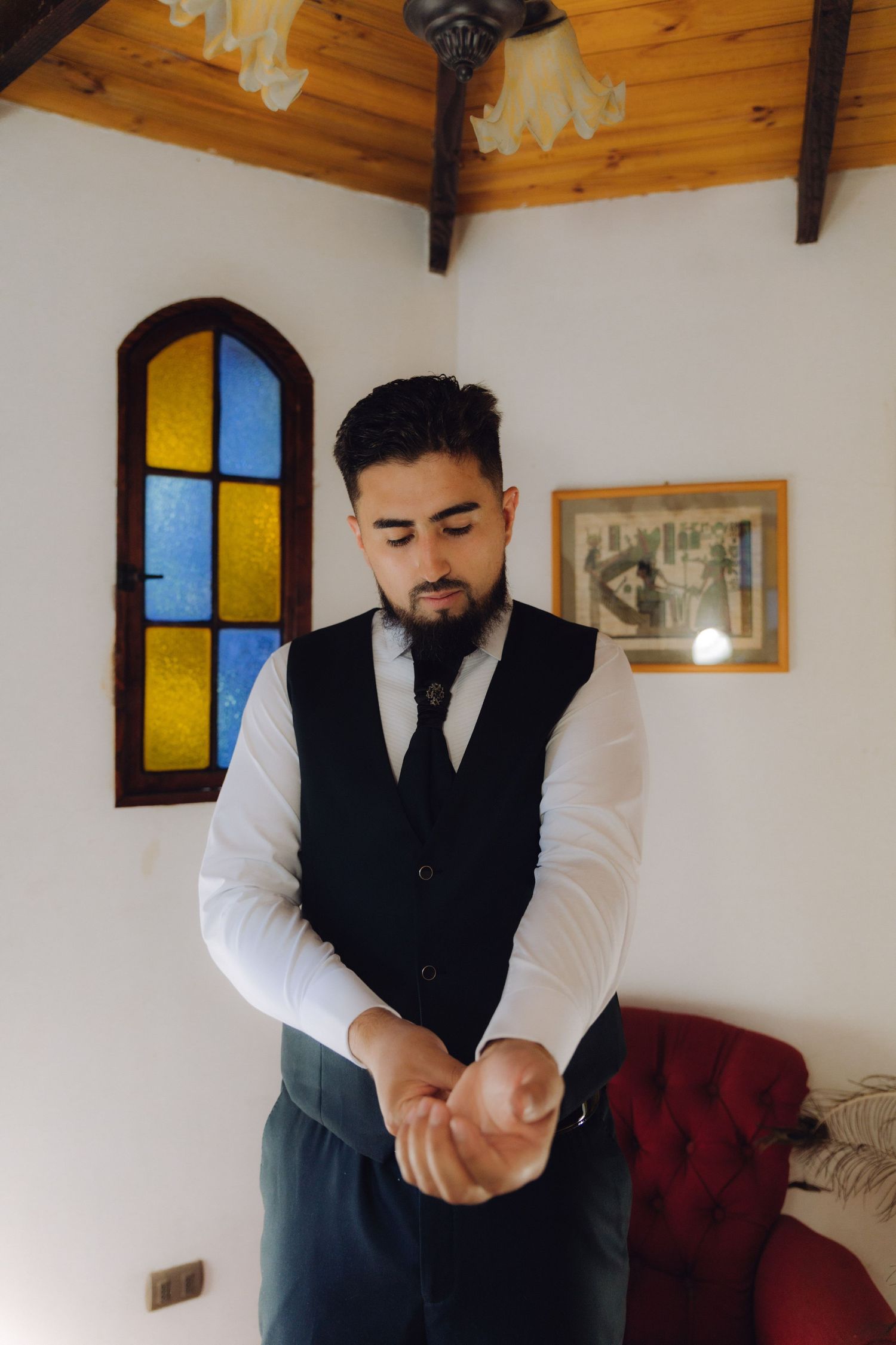 Bearded groom in white shirt and black vest adjusting cufflinks while getting ready for wedding.