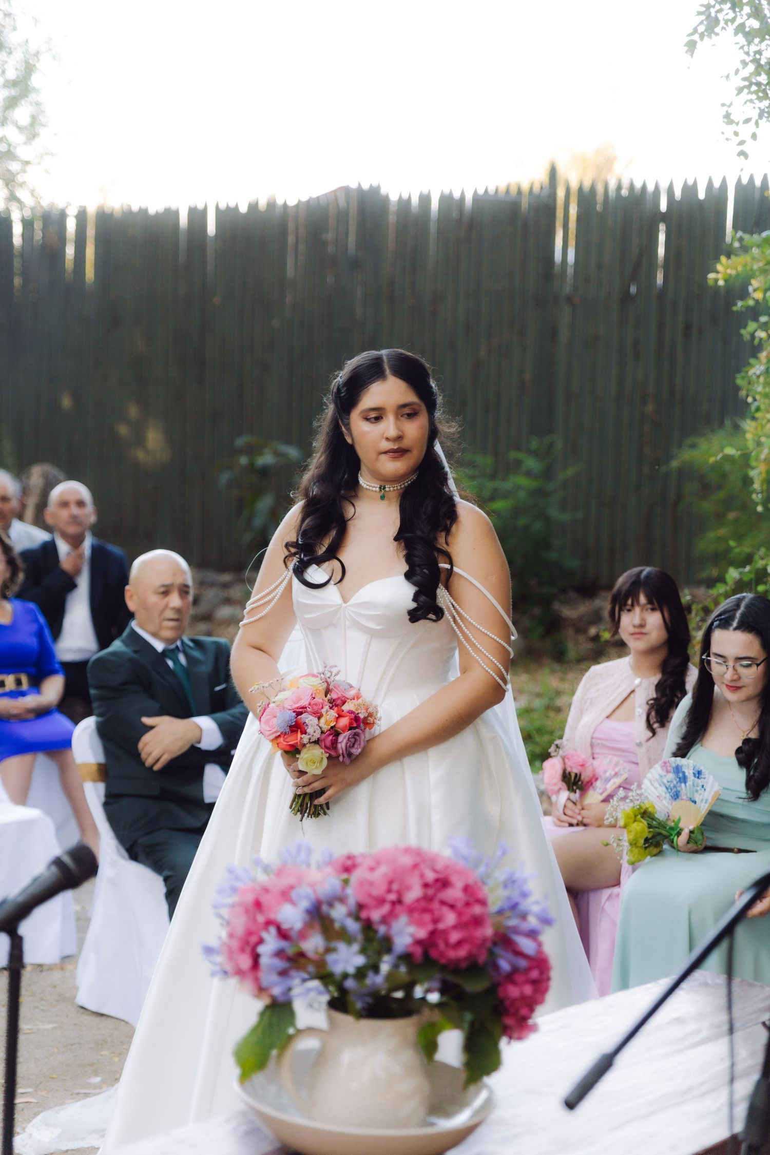 Beautiful bride in white ball gown holds vibrant pink bouquet while standing at outdoor wedding ceremony.