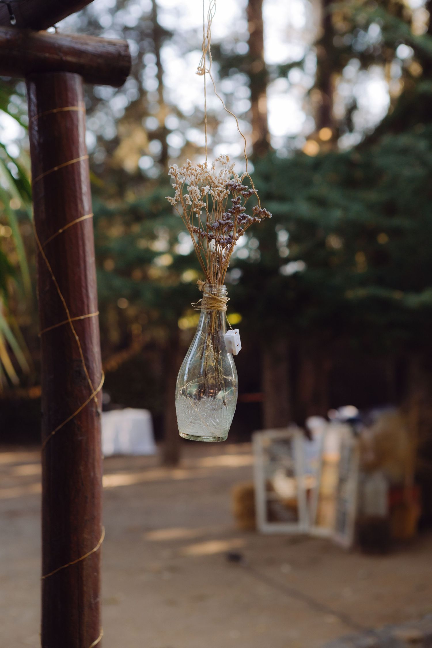 Rustic glass bottle vase with dried wildflowers hanging from twine at an outdoor wedding ceremony decoration.
