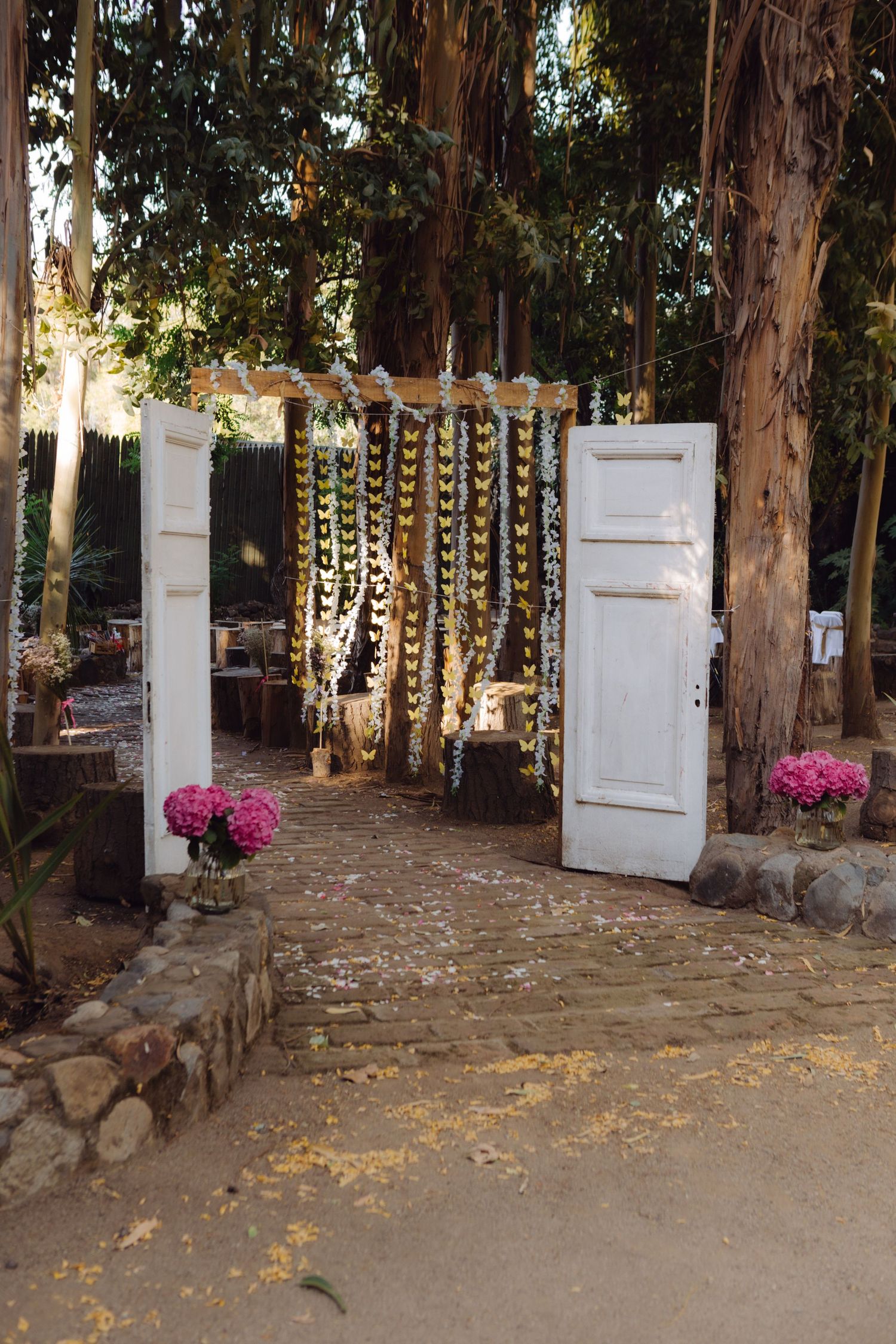 Elegant outdoor wedding entrance with white vintage doors, butterfly garlands, and pink flower arrangements.
